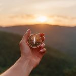 Female hand with compass in summer mountains at sunrise, pov.